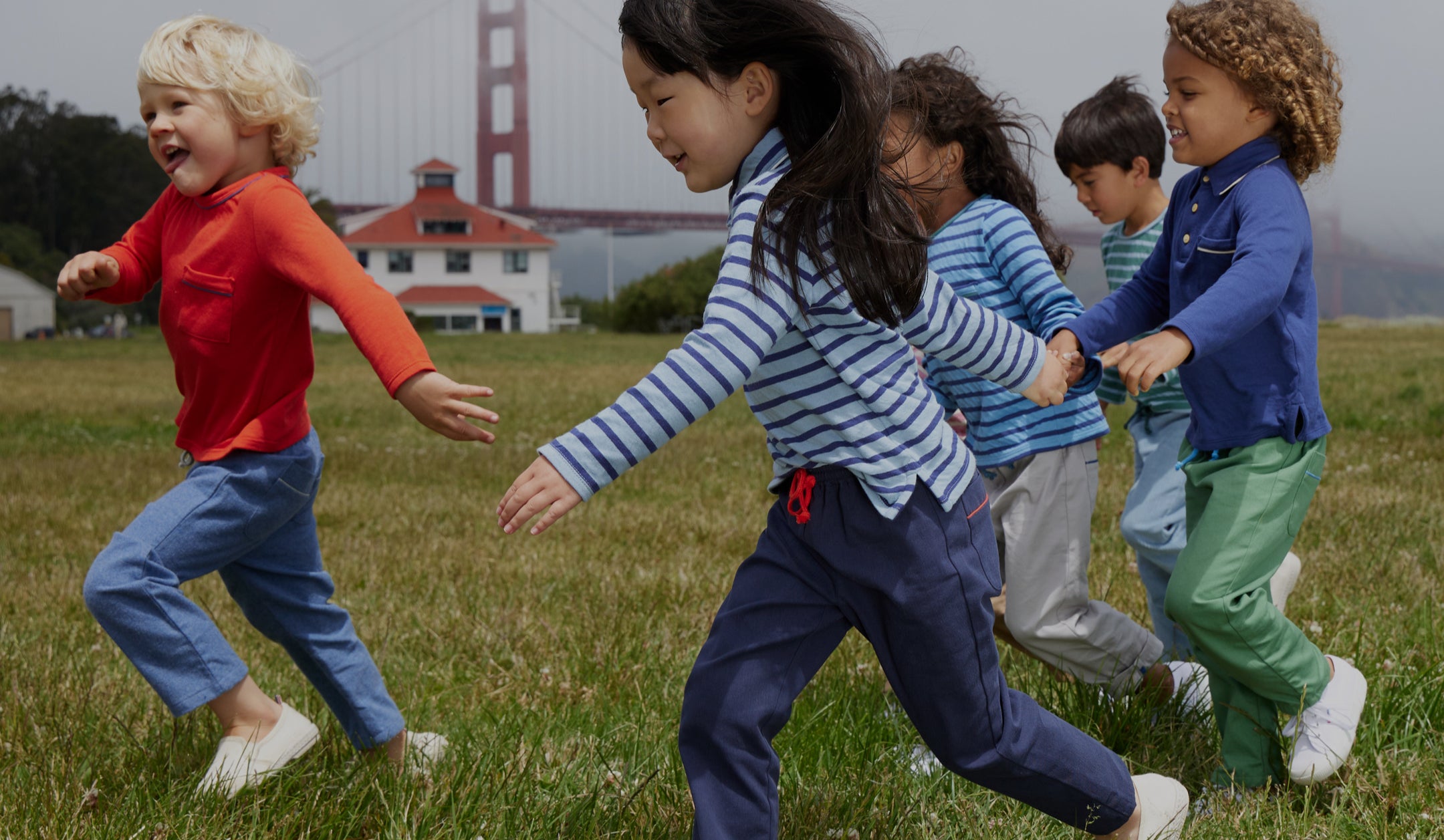 Five kids running in a field wearing Oso clothes with Golden Gate Bridge in the background.
