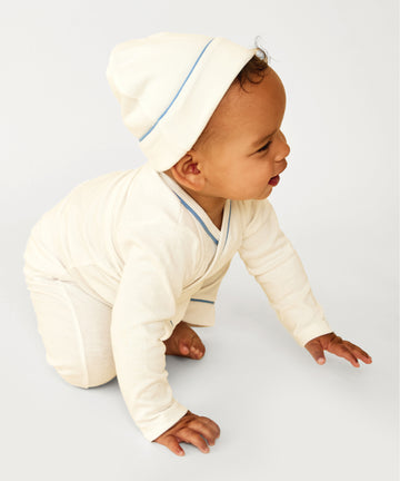Baby crawling on ground wearing crossbody onesie, leggings, and hat
