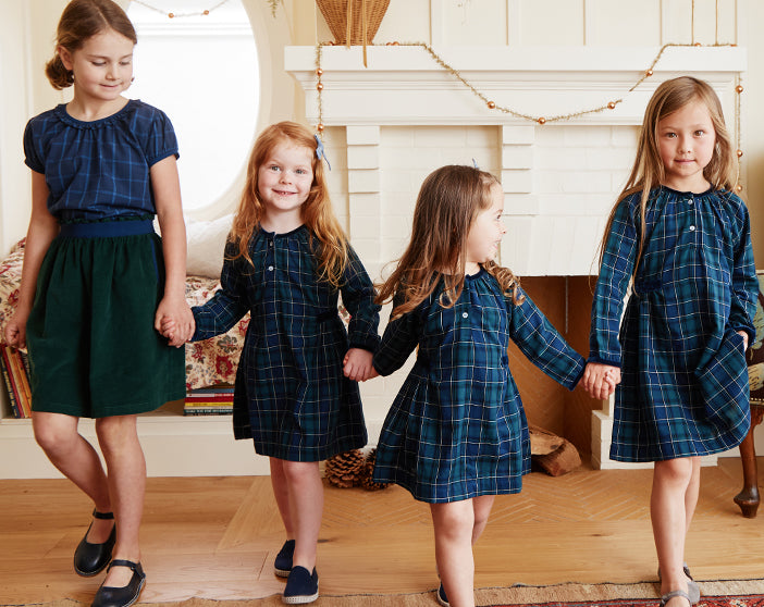 Four girls holding hands in front of a fireplace wearing Green Plaid Holiday Dresses and Skirt.